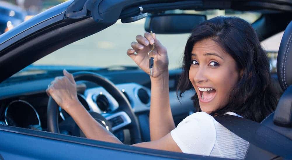 A smiling woman is sitting in a convertible car that she bought online.