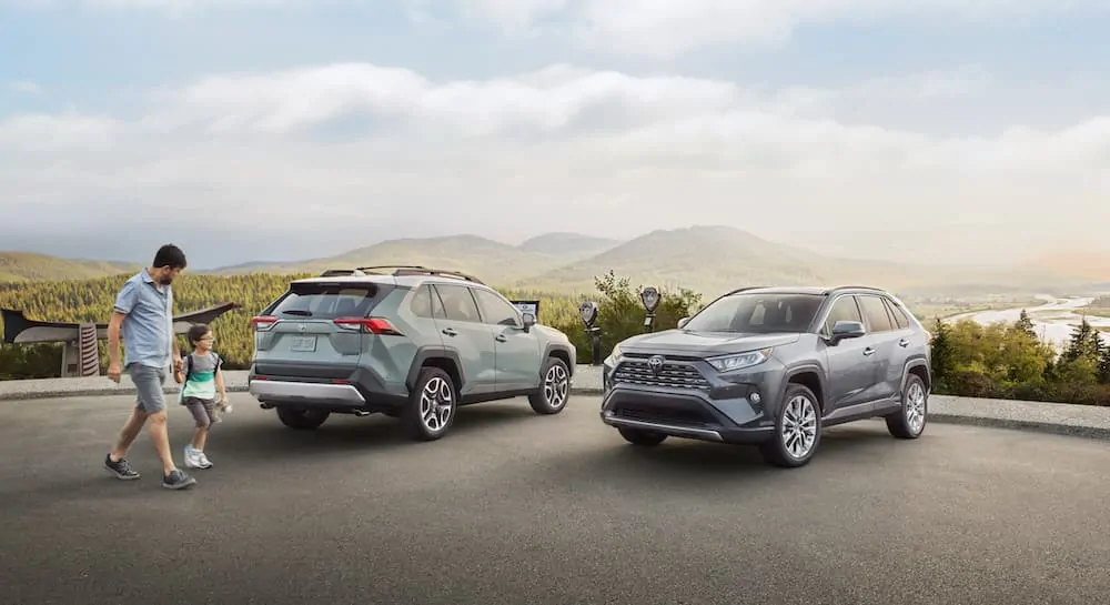 A dad and child are walking past blue and grey 2020 Toyota RAV4s with mountian views after leaving a Toyota dealership near me.