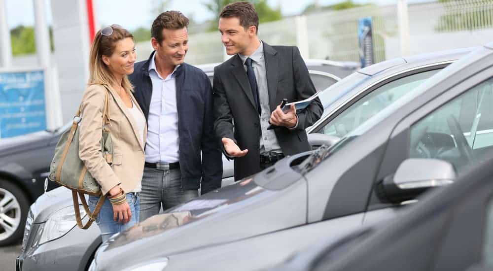 A salesman is showing a couple a grey used vehicle.