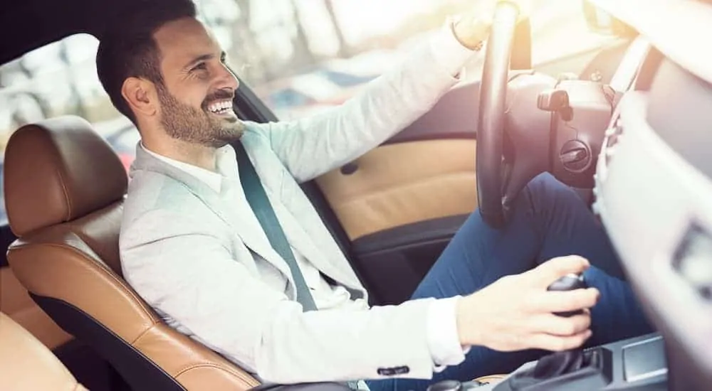 A man is enjoying a test drive in a black and tan interior of a used car.