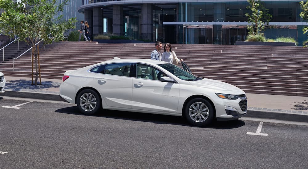 A white 2020 Chevy Malibu is parked on a city street in front of steps.