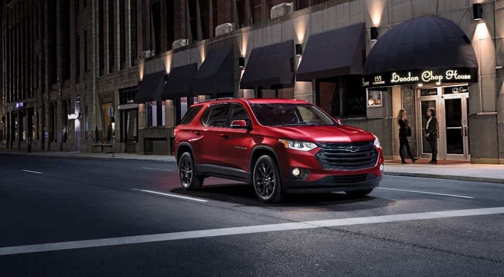 A red 2020 Chevy Traverse RS is parked in front of a city steak house at night.