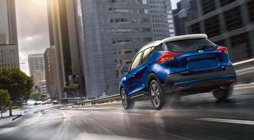 A blue 2020 Nissan Kicks is driving on a wet city street after losing the 2020 Chevy Trax vs 2020 Nissan Kicks comparison.