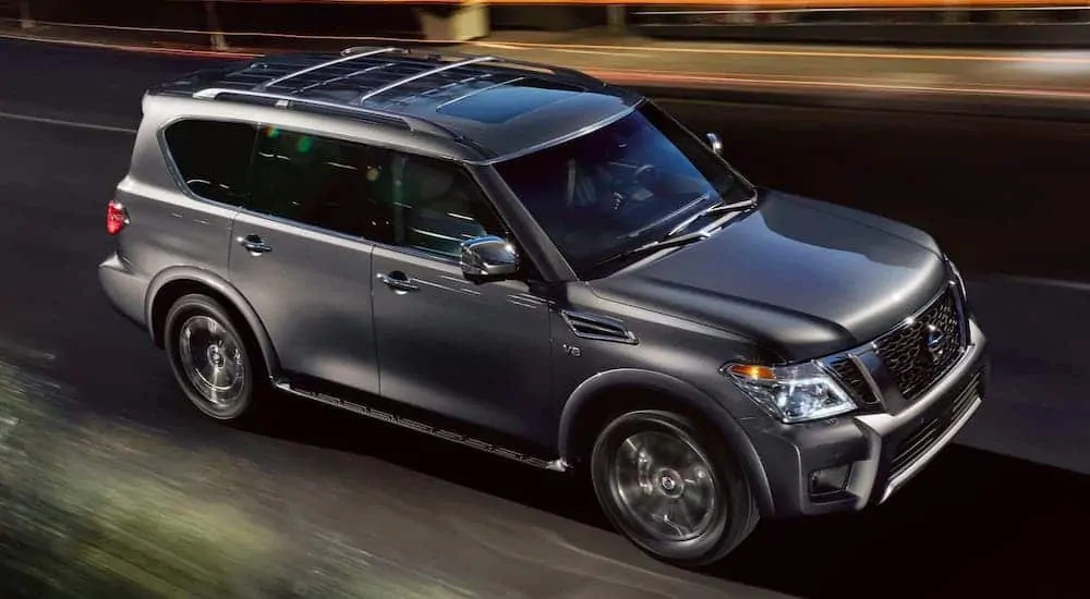A gray 2020 Nissan Armada is driving on a city street at night.