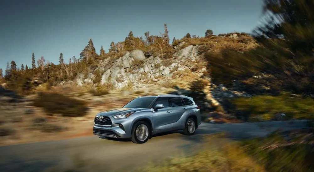 A blue/gray 2020 Toyota Highlander is driving on a road past large rocks.