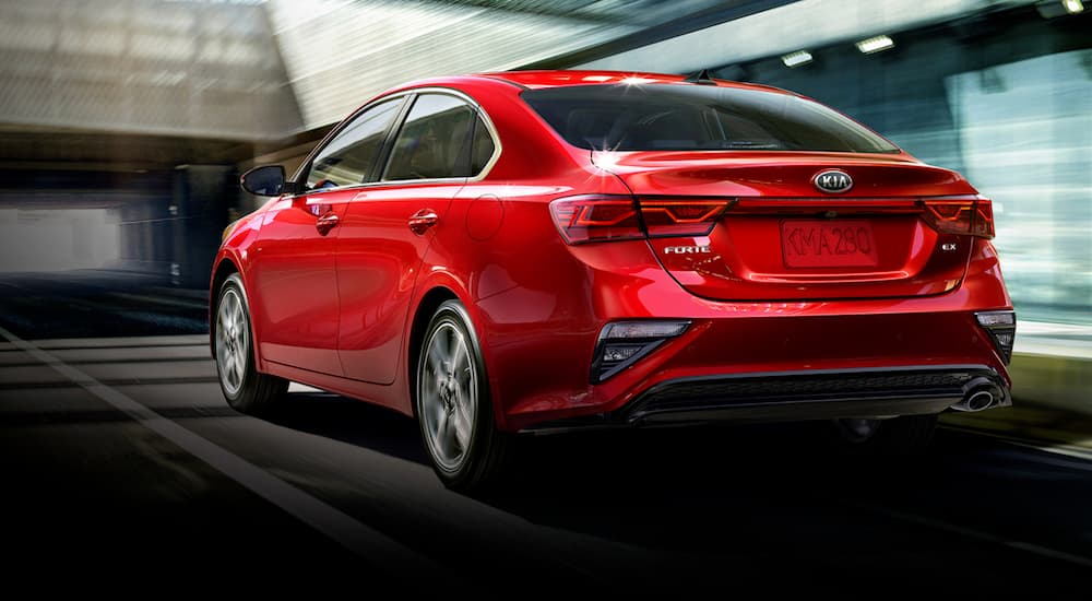 A red 2020 Kia Forte is driving toward a tunnel on a highway.