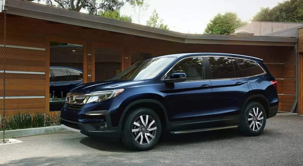 A blue 2020 Honda Pilot is parked outside a modern home.