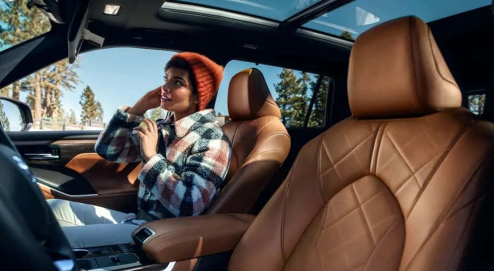 A woman is sitting in the brown leather interior of a 2020 Toyota Highlander Hybrid.