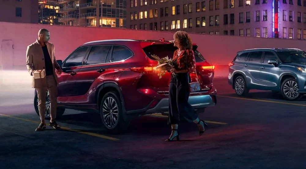 A couple is next to a red 2020 Toyota Highlander Hybrid in a city parking garage at night.