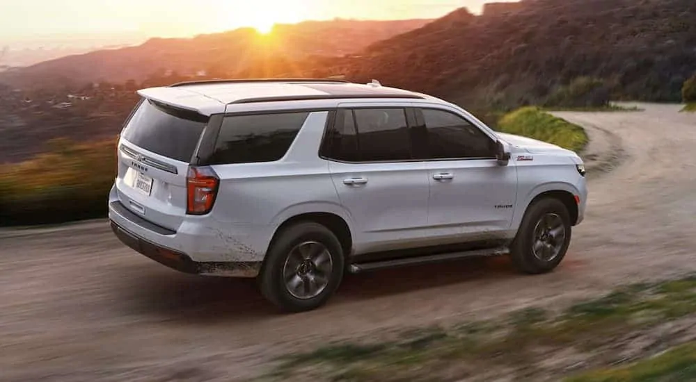 A white 2021 Chevy Tahoe is driving on a dirt road with a sunset view.