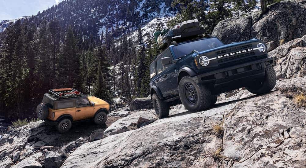 A black and an orange 2021 Ford Bronco are off-roading up a rocky mountain.