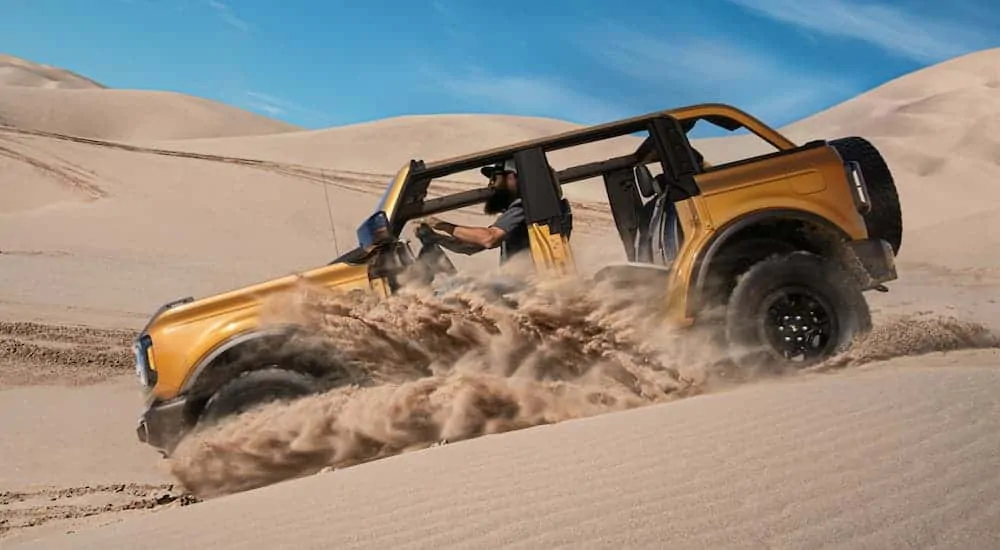 An orange 2021 Ford Bronco is shown from the side off-roading on a sand dune.