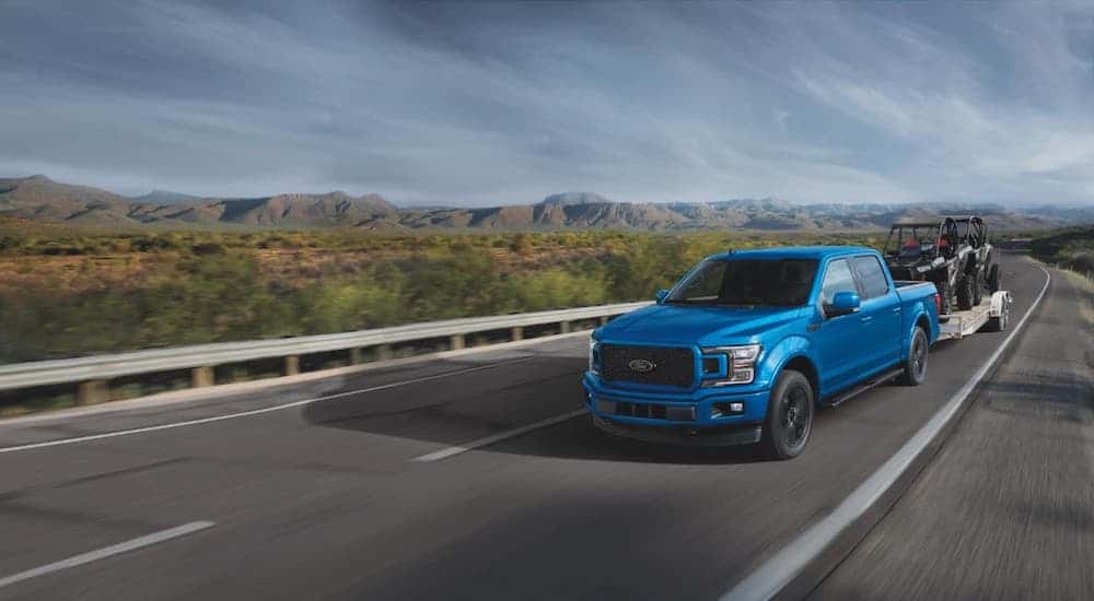 A blue 2020 Ford F-150 is towing a trailer on a highway.