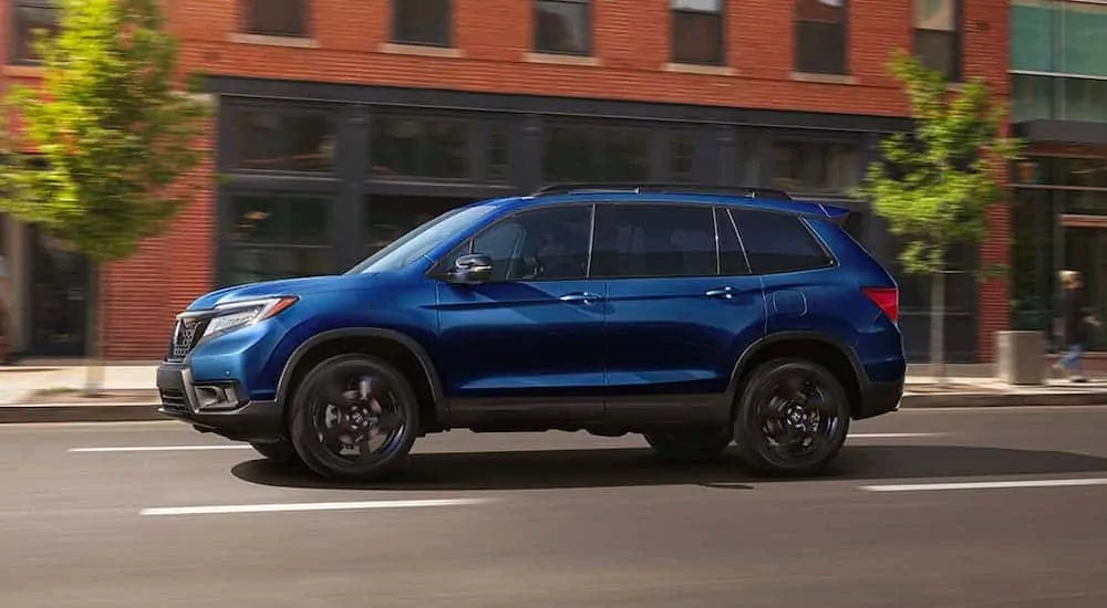 A blue 2020 Honda Passport Elite is driving on a city street and shown from the side.