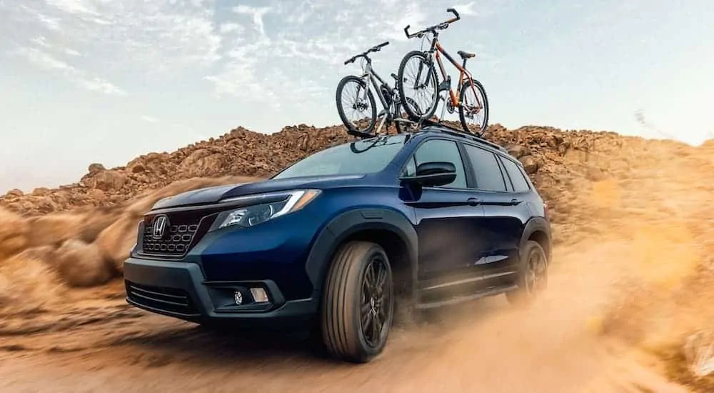 A blue 2020 Honda Passport is driving in the desert with bikes on the roof.