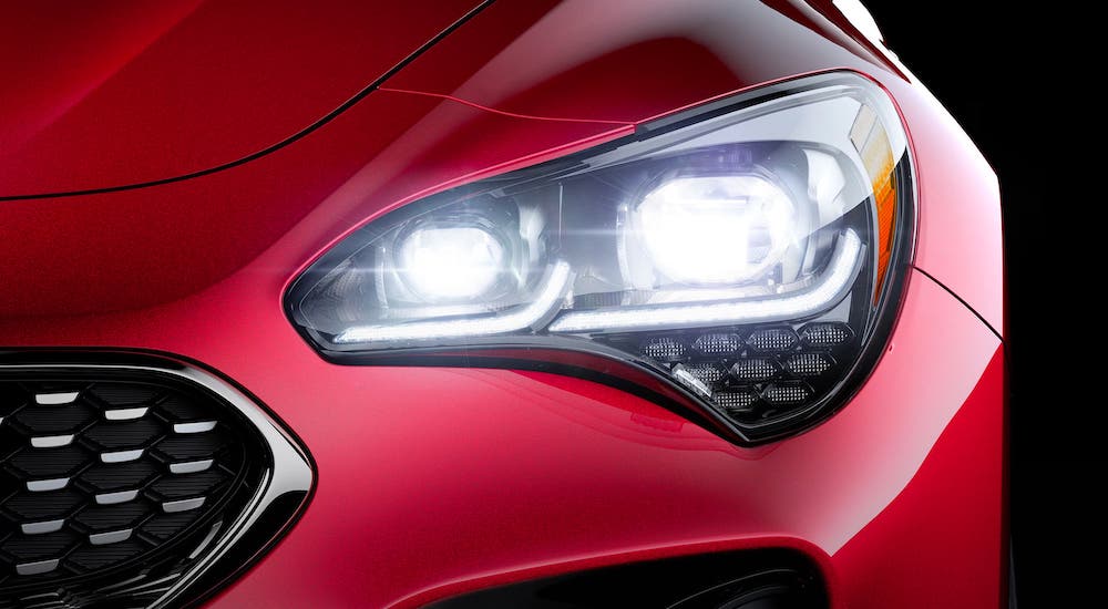 A closeup shows the headlight and grille of a red 2020 Kia Stinger.