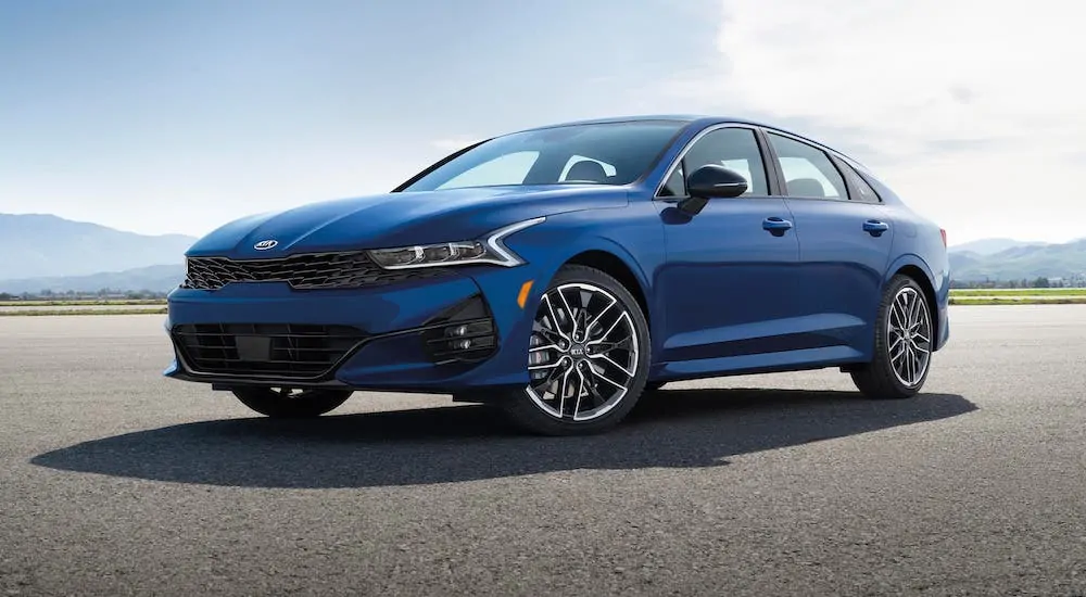 A blue 2021 Kia K5 is parked on an empty track.