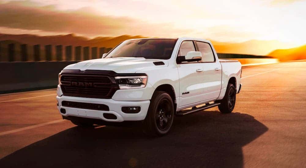 A white 2020 Ram 1500 Black Edition is driving on an empty road at sunset.