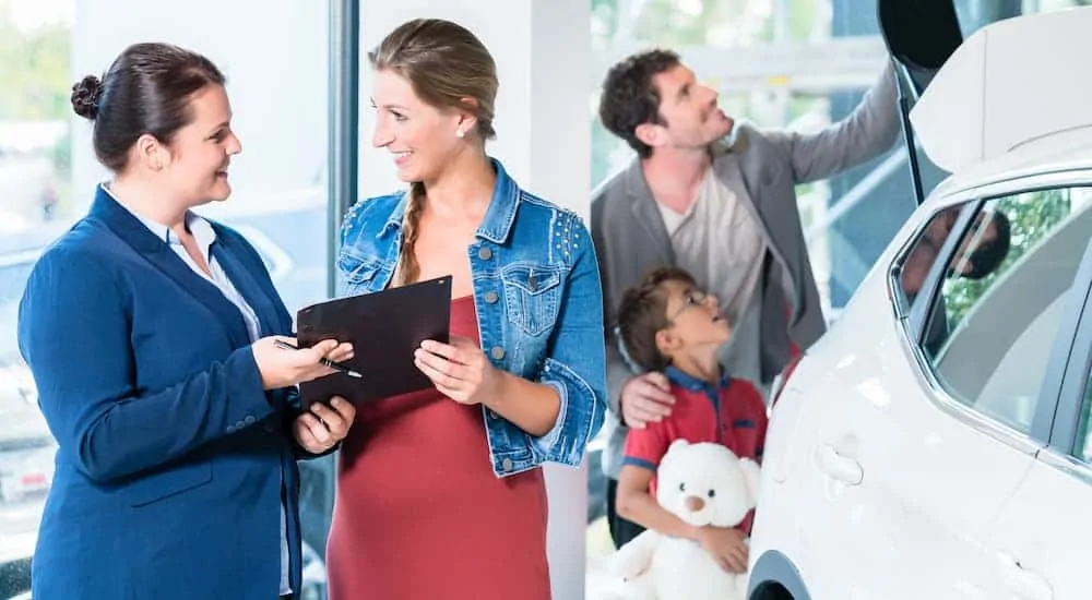 A family is looking at a white used car in Cincinnati and talking with a saleswoman.