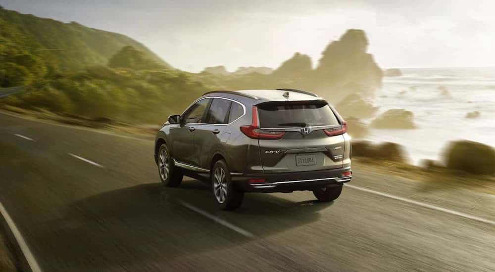 A grey 2020 Honda CR-V Hybrid is driving past a rocky ocean bay.