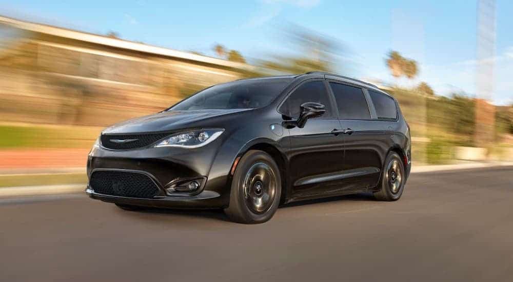 A black 2020 Chrysler Pacifica is driving on a road with a blurry background.