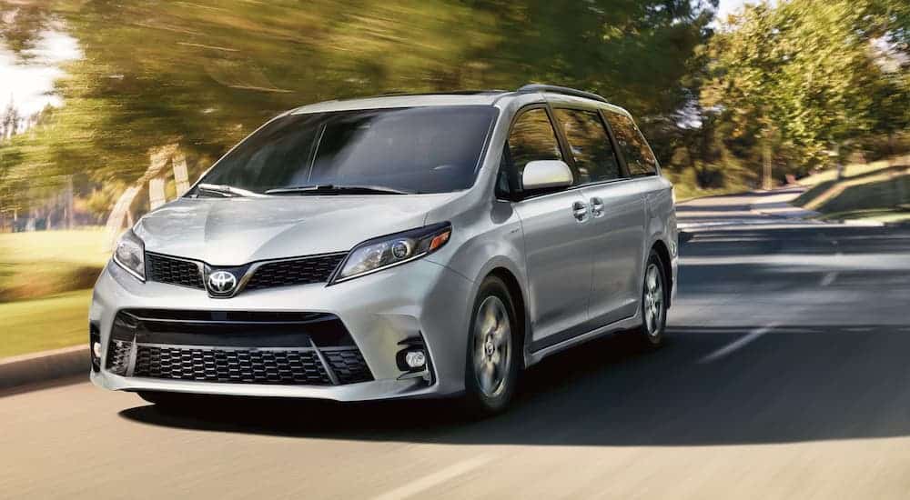 A silver 2020 Toyota Sienna is driving on a tree-lined road.