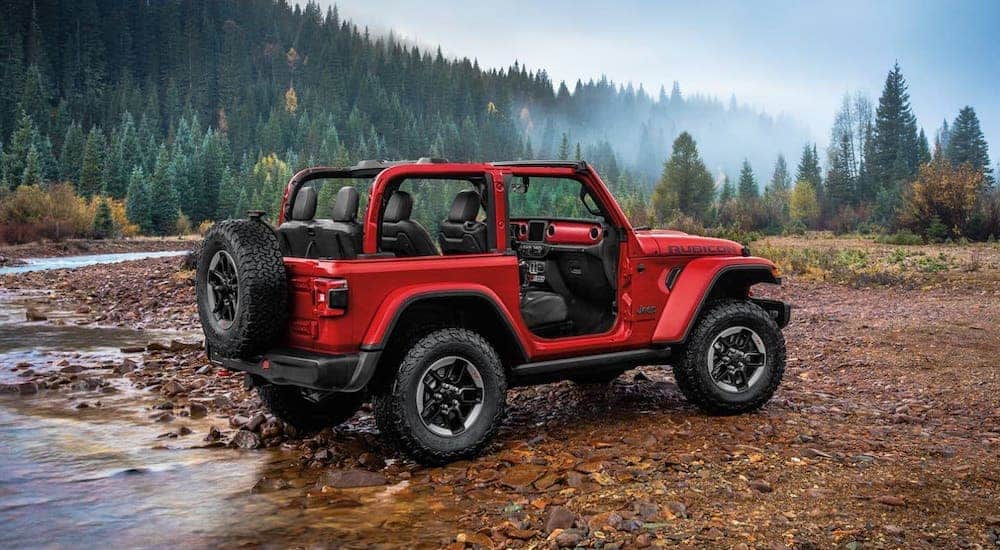 A red 2020 Jeep Wrangler is crossing a river in the woods.