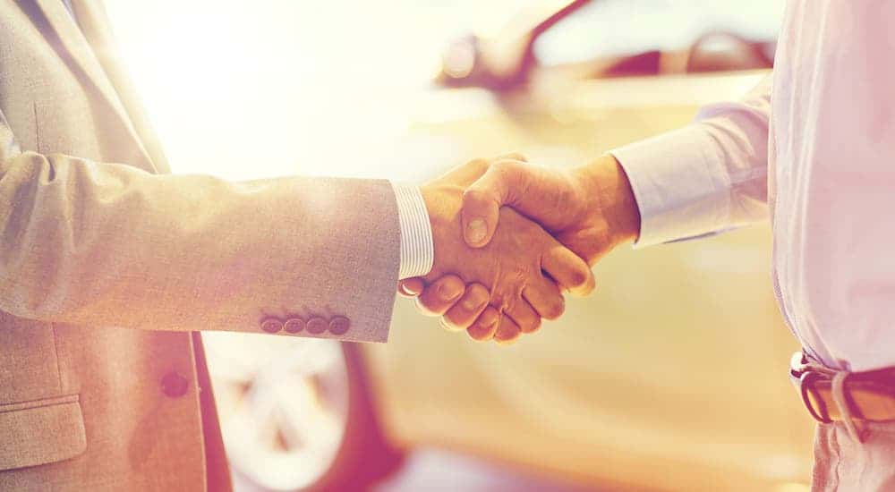 A closeup shows 2 hands shaking at a car dealership.