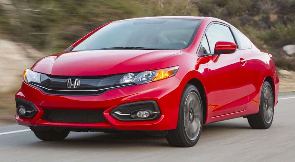 A red 2015 Honda Civic is driving past blurred trees.