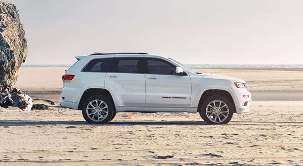 A white 2020 Jeep Grand Cherokee is parked on a beach and shown from the side.