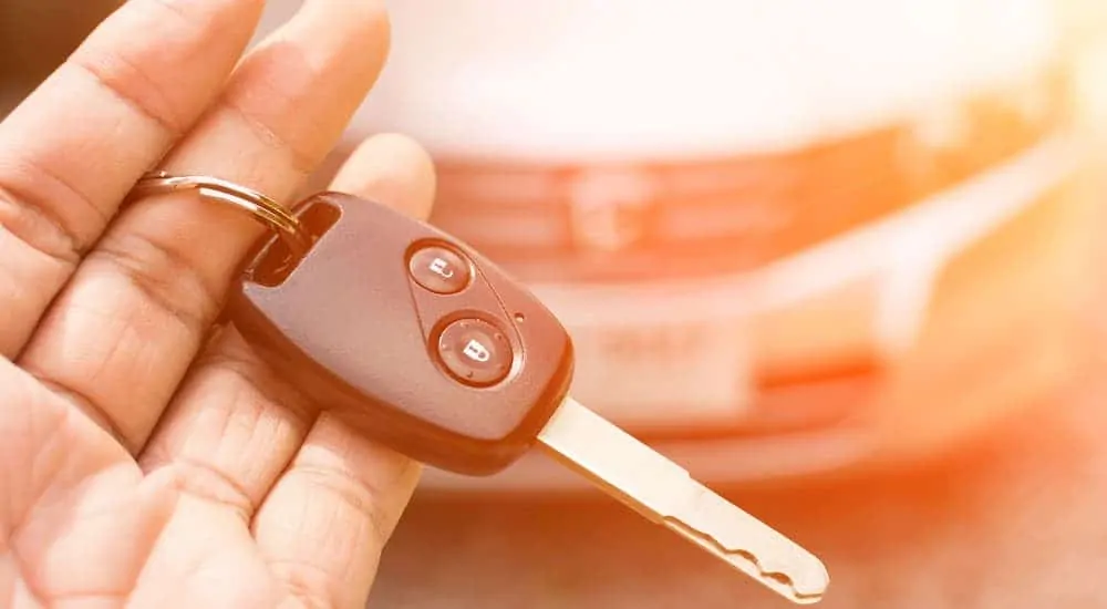 A hand is holding a car key in front of an out of focus car.