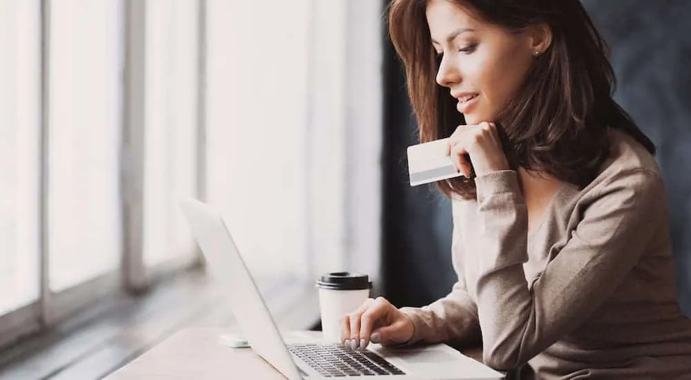 A woman is shopping for Online Car Dealerships on her laptop and holding a credit card.
