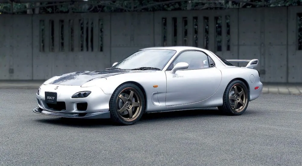 A silver 2003 Mazda RX-7 is parked in front of a concrete structure.