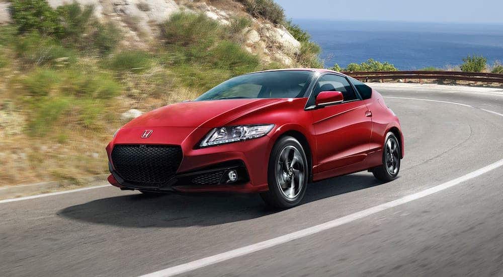 A red 2016 Honda CR-Z is driving around a coastal highway.