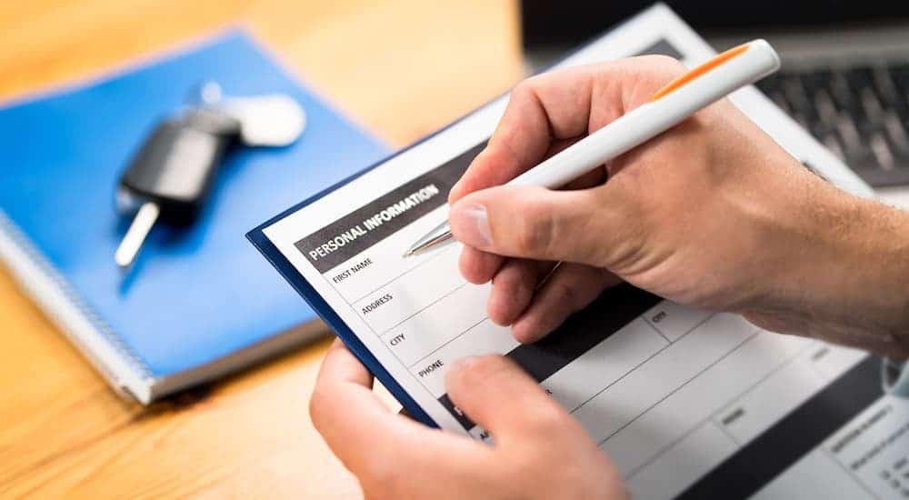A closeup shows hands filling out paperwork in front of a blue binder with a car key on it.