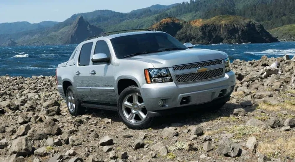 A silver 2013 Chevy Avalanche is driving over rocks.