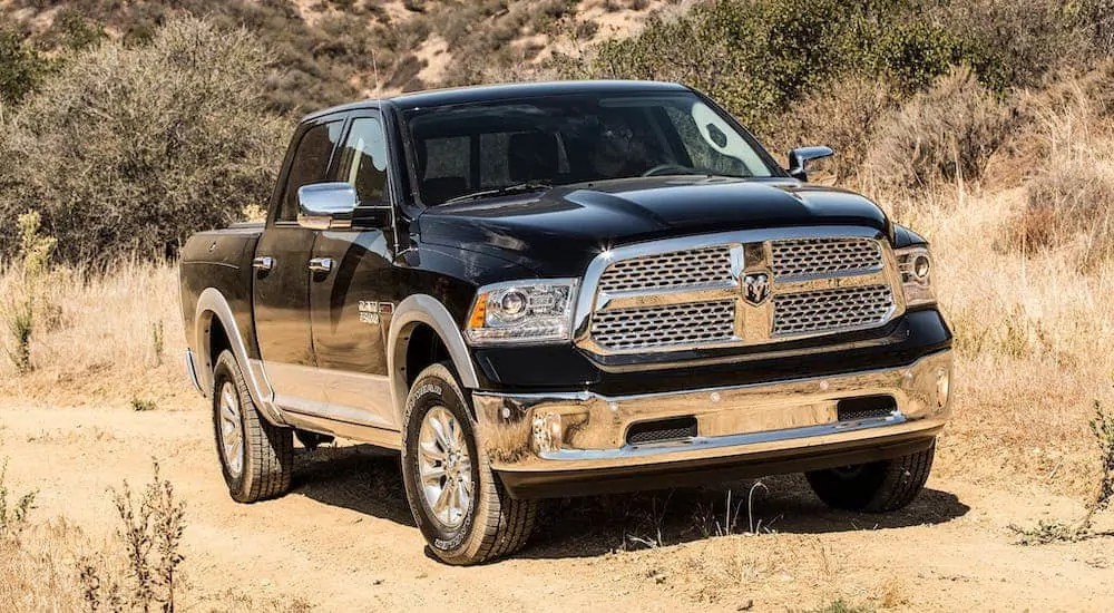 A popular used truck for sale, a black 2017 Ram 1500, is driving on a dirt road.