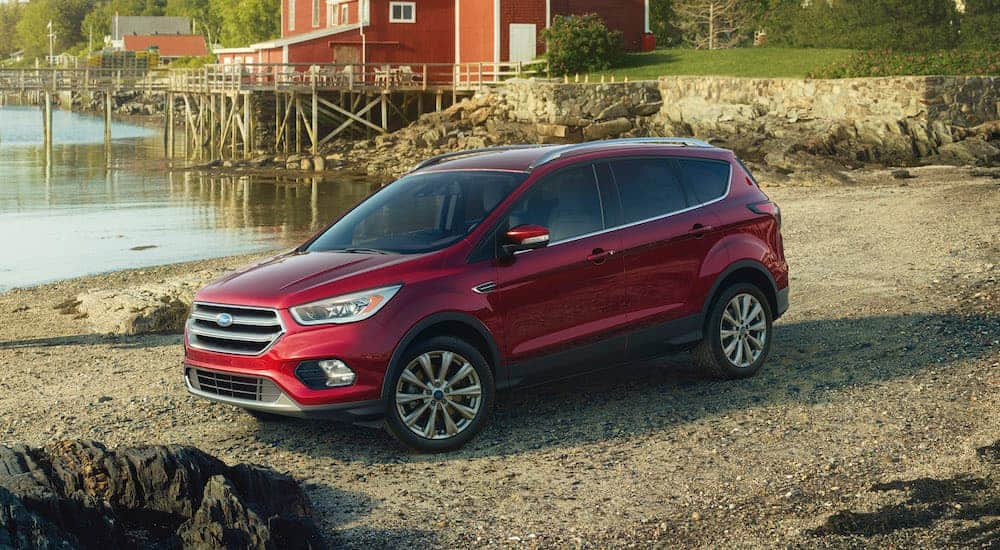 A red 2017 used Ford Escape is parked on a rocky shore in front of a red building.