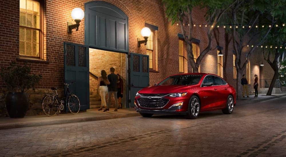 A red 2020 Chevy Malibu is parked in front of a brick building at night after winning the 2020 Chevy Malibu vs 2020 Nissan Altima comparison.