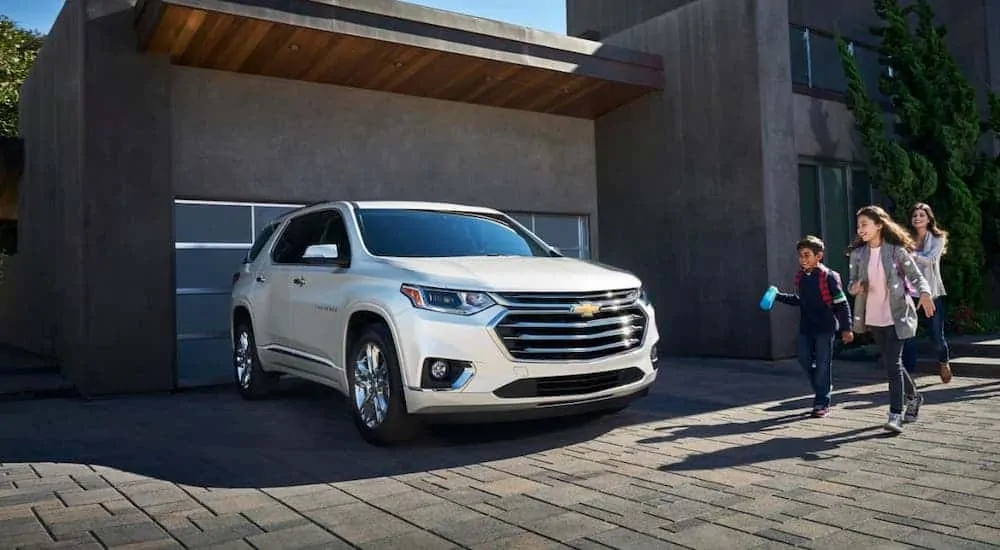 A family is walking towards a white 2020 Chevy Traverse that is parked in their driveway.