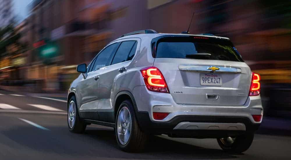 A white 2020 Chevy Trax is driving away on a city street at night.