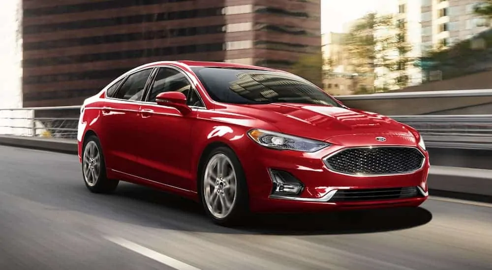 A red 2020 Ford Fusion is driving on a city street.