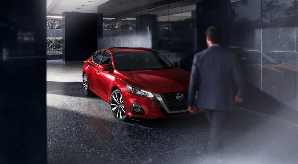 A man is walking towards a red 2020 Nissan Altima after losing the 2020 Ford Fusion vs 2020 Nissan Altima comparison.