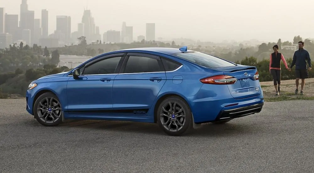 A blue 2020 Ford Fusion is parked in front of a hazy city.