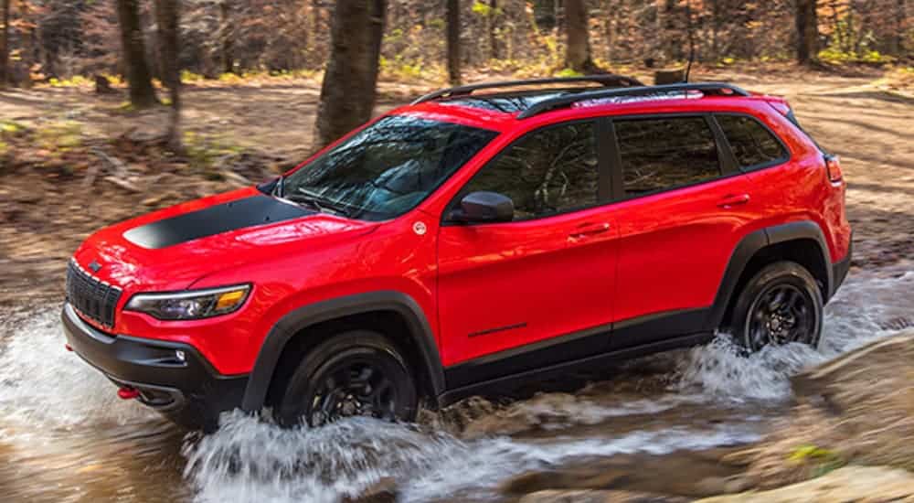 A red 2020 Jeep Cherokee Trailhawk is off-roading through a river.