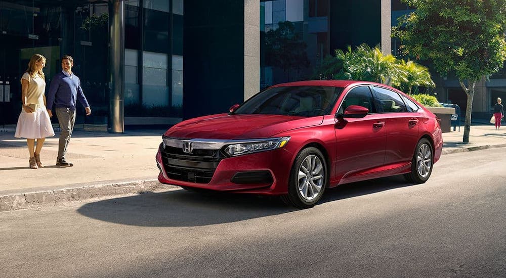 A couple is walking towards a red 2020 Honda Accord that is parked on a city street after losing the 2020 Kia Optima vs 2020 Honda Accord comparison.