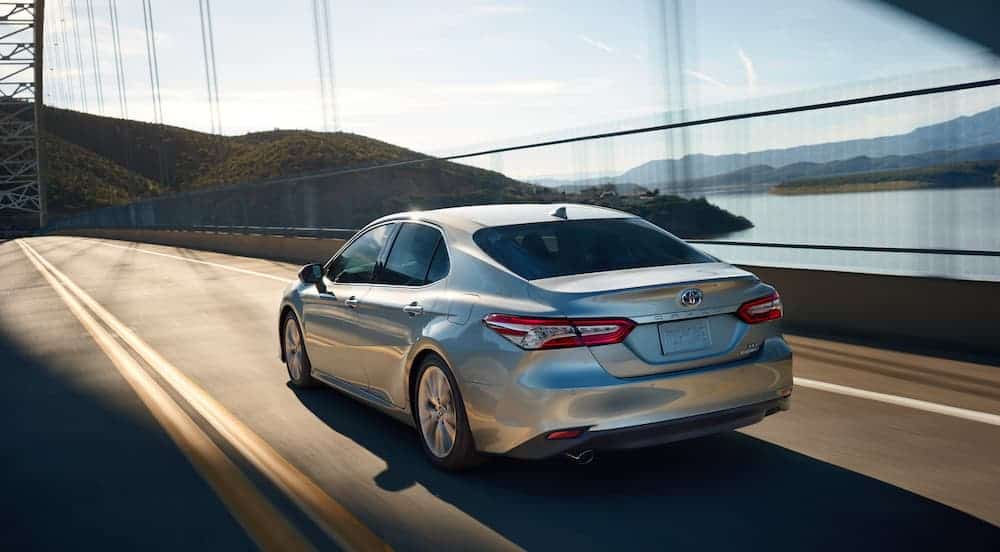 A silver 2020 Toyota Camry is driving away on a bridge next to water.