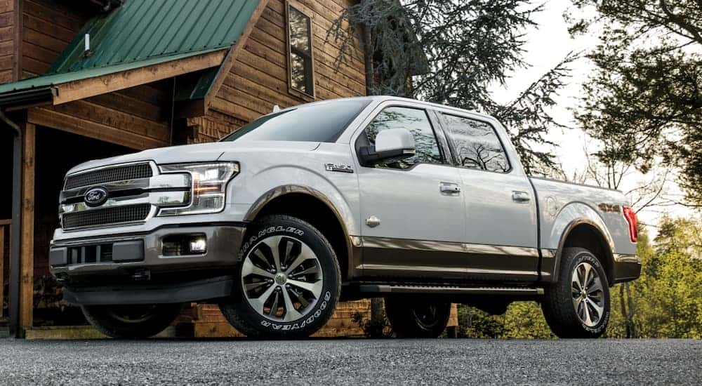 A white 2020 Ford F-150 King Ranch is parked in front of a log cabin.