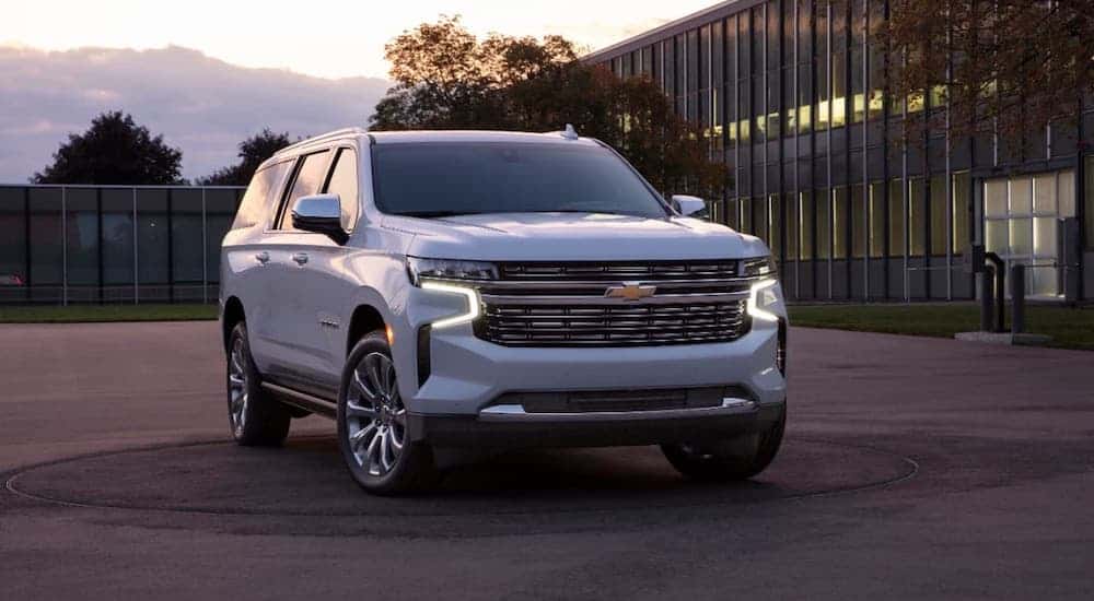 A white 2021 Chevy Suburban is parked in front of a glass building at sunset.