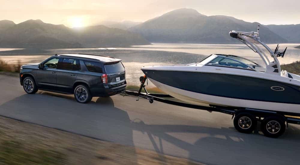 A grey 2021 Chevy Tahoe is towing a boat past a lake and mountains.